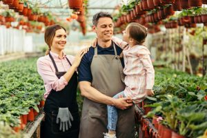 Happy family communicating while working in their greenhouse. Father is holding little girl in his arms.